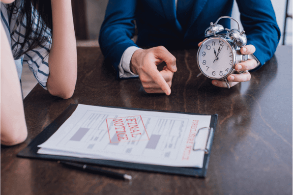 A man holding an alarm clock, showing a woman a debt recovery letter that is due, saying final notice that a creditor has written themselves to the debtor. 